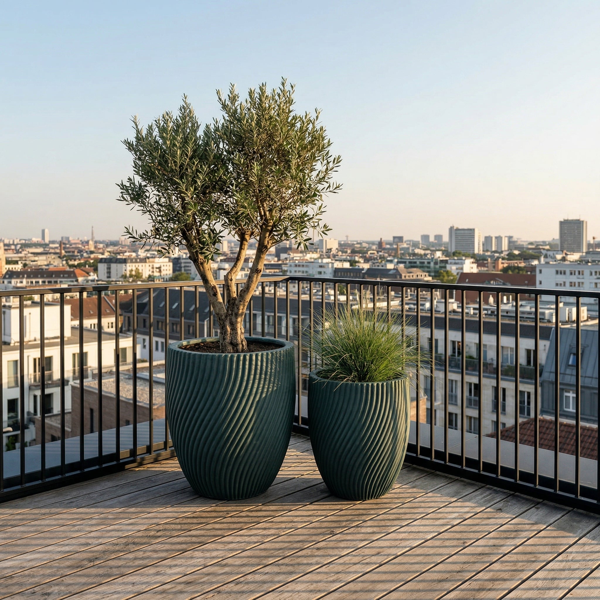 Detailní pohled na velký betonový květináč Solstice - Tmavě zelená s okrasnou rostlinou na dřevěné podlaze moderní městské střešní terasy.