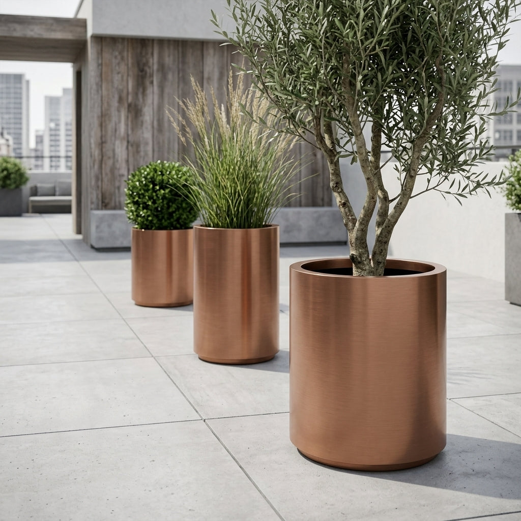 Detailní pohled na velký květináč z nerezové oceli Metropole v měděné barvě s olivovníkem na moderní městské terase.