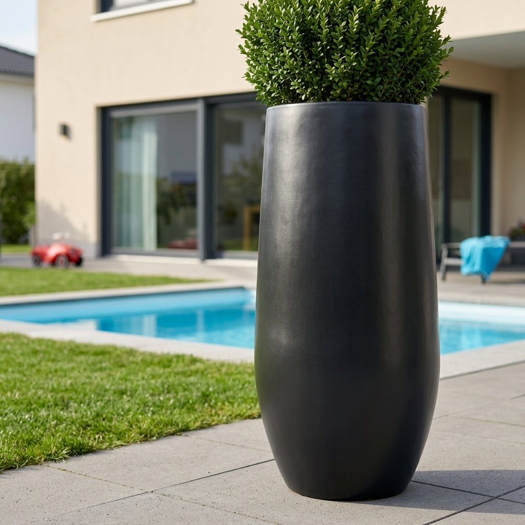 Detailní pohled na matně černý betonový květináč Zenith XL s keřem na moderní rodinné terase u bazénu.