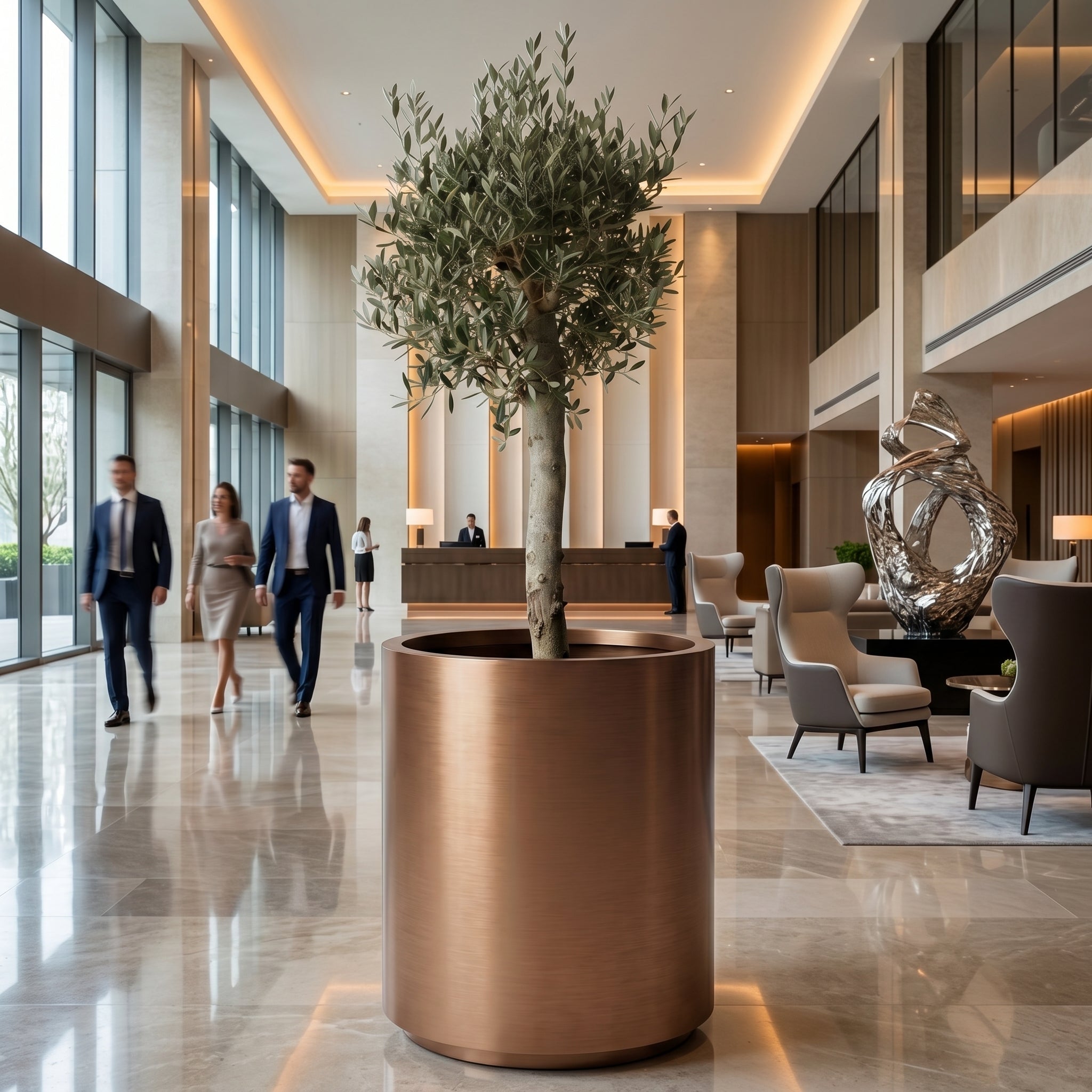 Olivovník se silným kmenem v měděném květináči METROPOLE 60×70 cm v interiéru luxusního hotelového lobby.