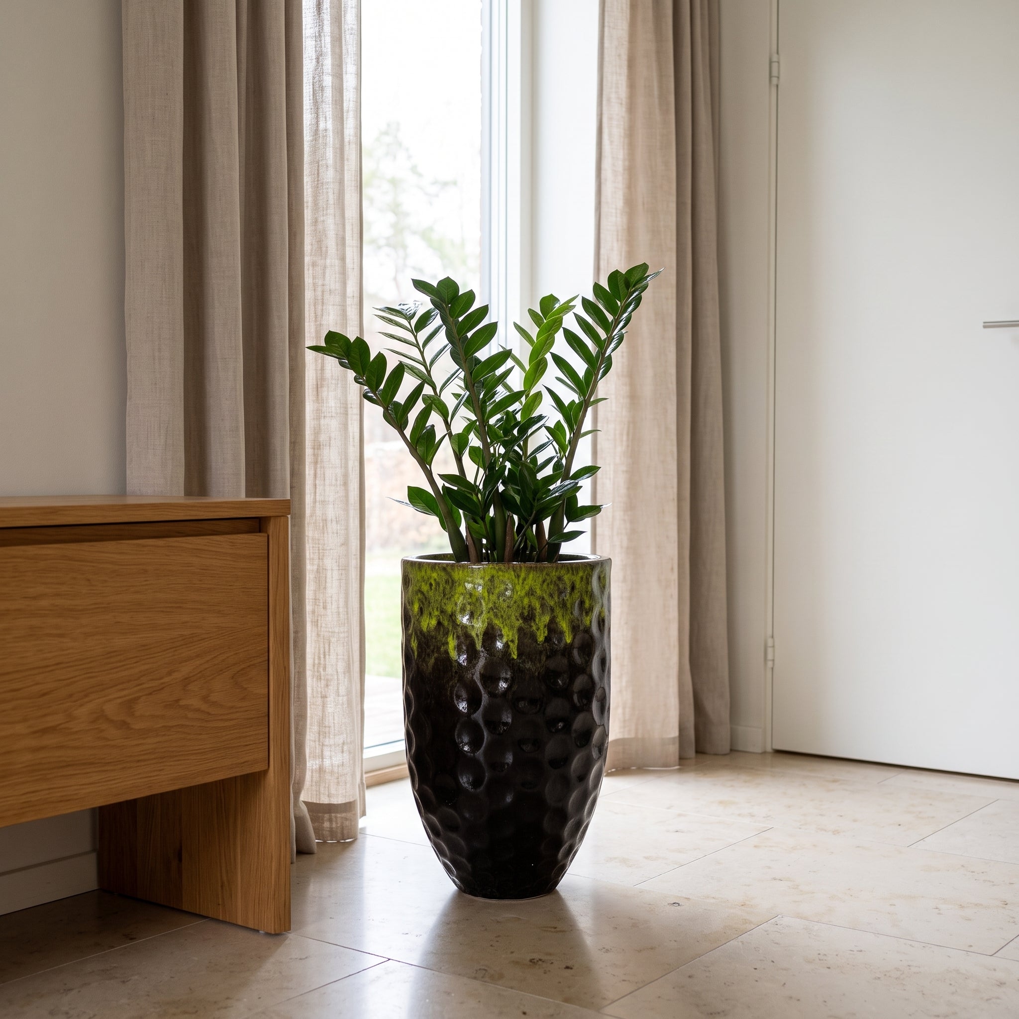 Černo zelený keramický květináč MEROVEE velikosti L (30 x 45 cm) s rostlinou Zamioculcas v luxusním skandinávském interiéru.