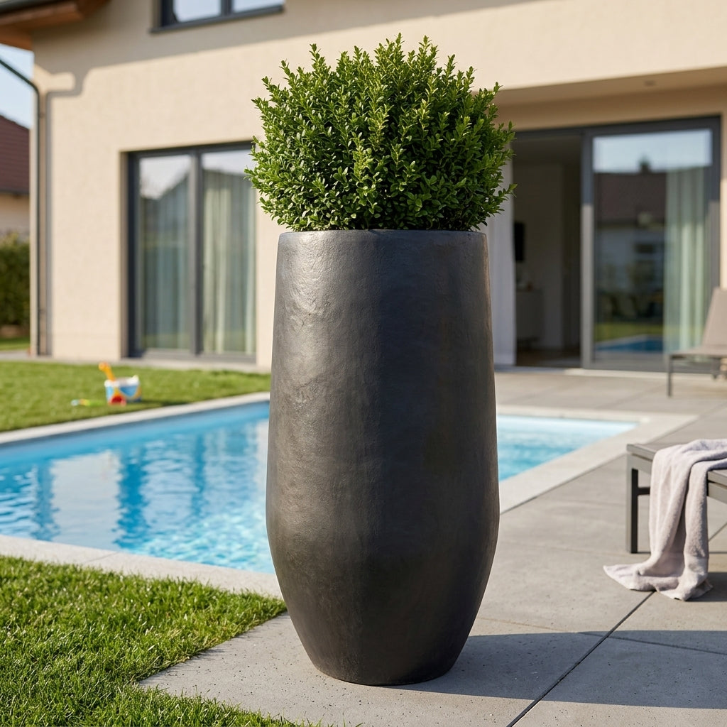 Detail na hnědý betonový květináč Zenith XL (30 cm x 60 cm) osázený keřem na moderní rodinné terase u bazénu.