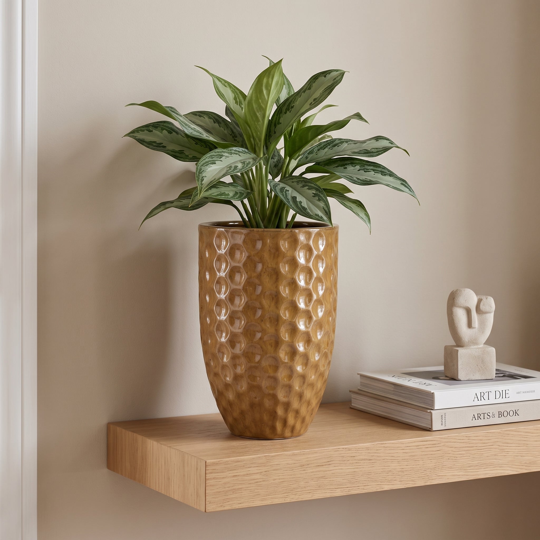 Keramický květináč MEROVEE - Pouštní žlutá - M (23 x 35 cm) s rostlinou Aglaonema na dřevěné polici v luxusním skandinávském interiéru.